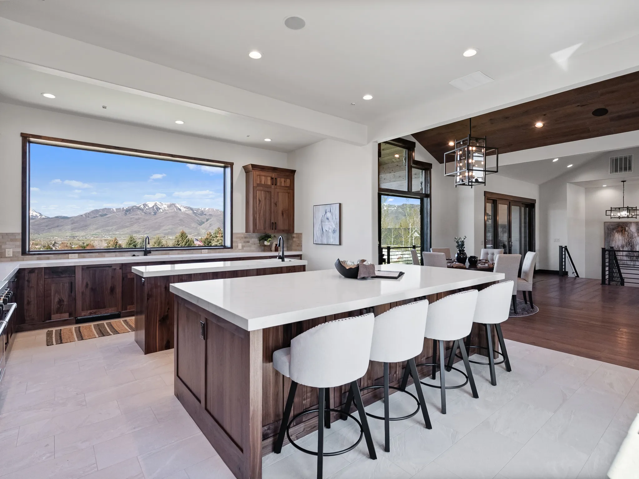 Gourmet kitchen with a large picture window, a substantial island with countertop seating, rich wood-finish cabinetry, light-toned tile flooring, and integrated ceiling lighting
