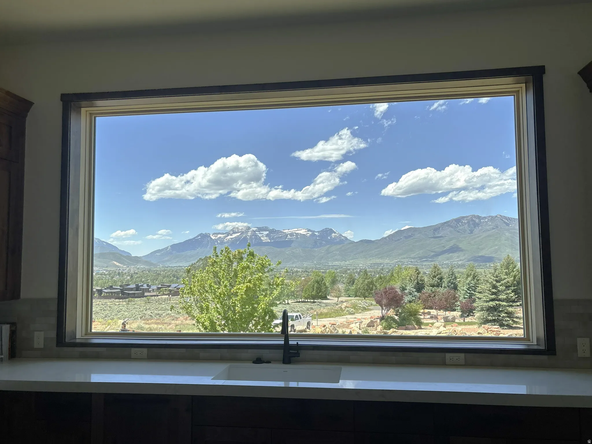 Panoramic window with mountain and valley scenery, featuring a white undermount sink, a matte black gooseneck faucet, light-colored countertops, and a subway tile backsplash