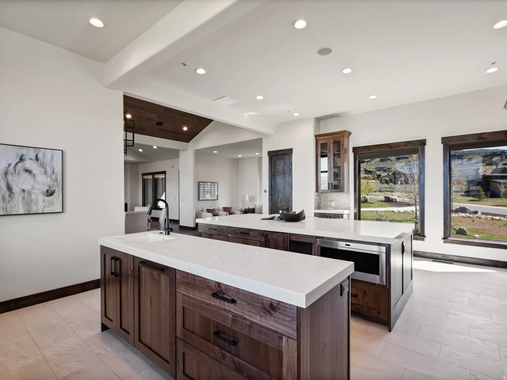 Kitchen featuring glass insert cabinets, lofted ceiling with beams, light stone countertops, recessed lighting, and open floor plan