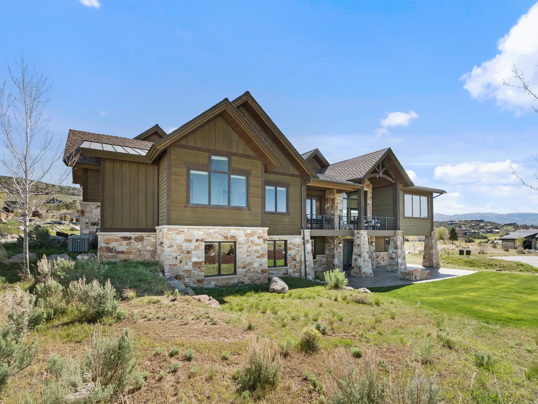 View of front of home featuring stone siding, a balcony, a front lawn, and a mountain view