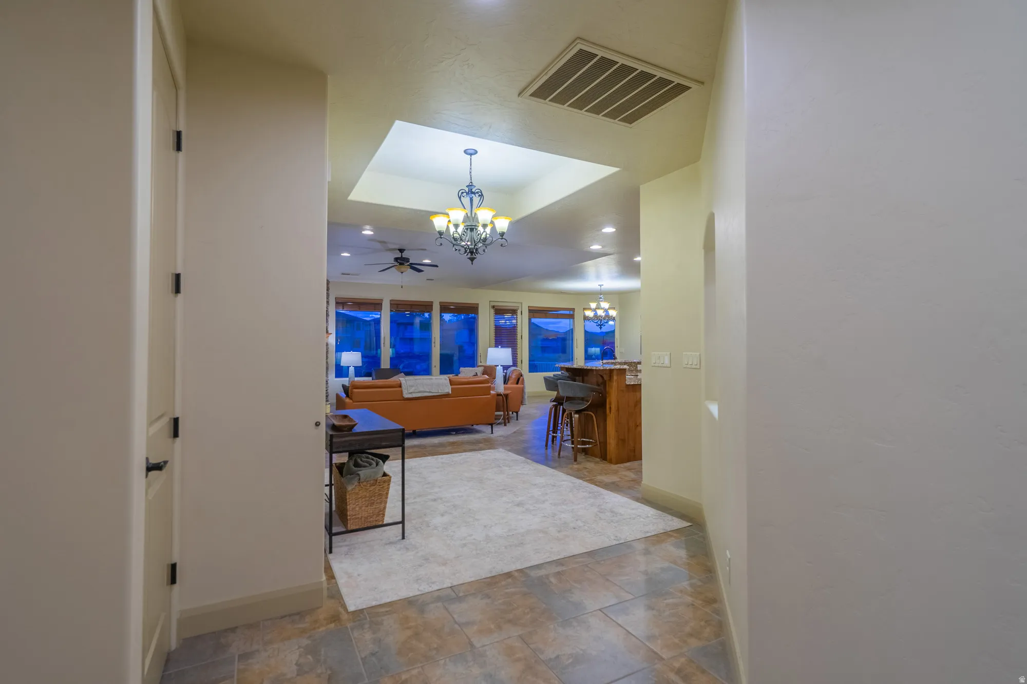 Living area featuring a tray ceiling, a chandelier, stone finish floors, and a ceiling fan