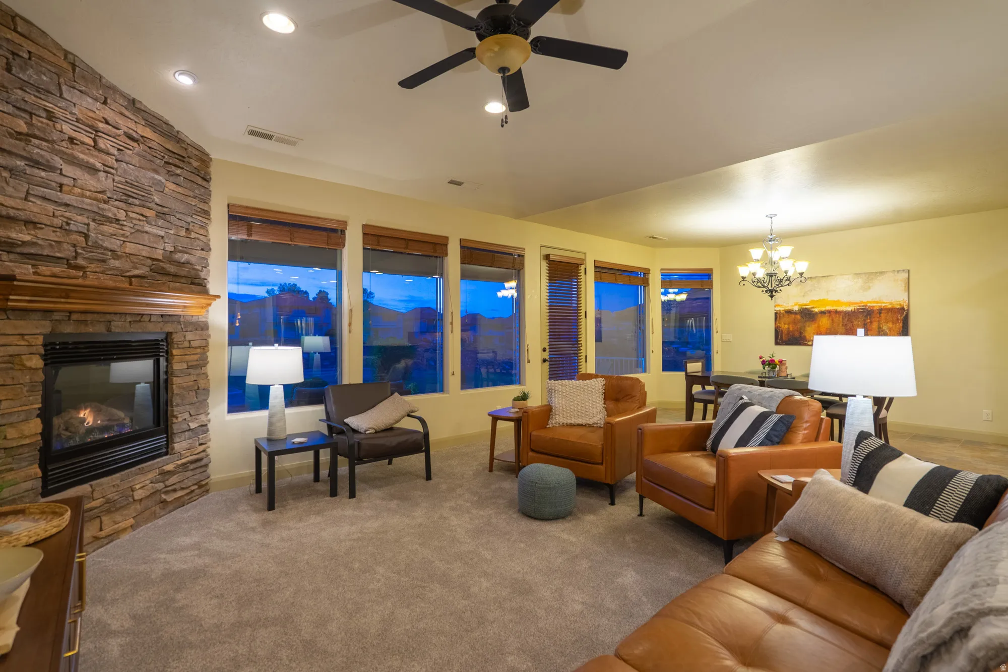 Carpeted living area with suspended lighting, a ceiling fan, and a stone fireplace