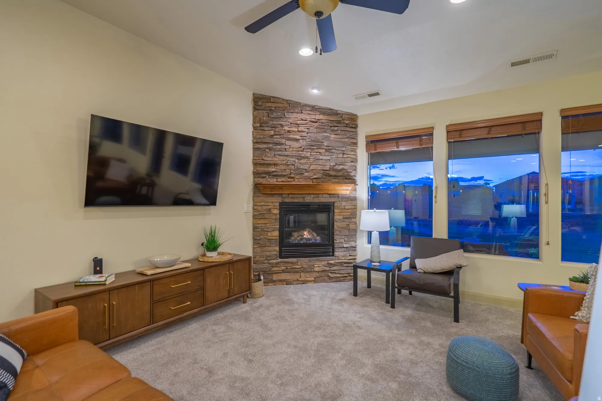 Living room with a fireplace, light colored carpet, and a ceiling fan