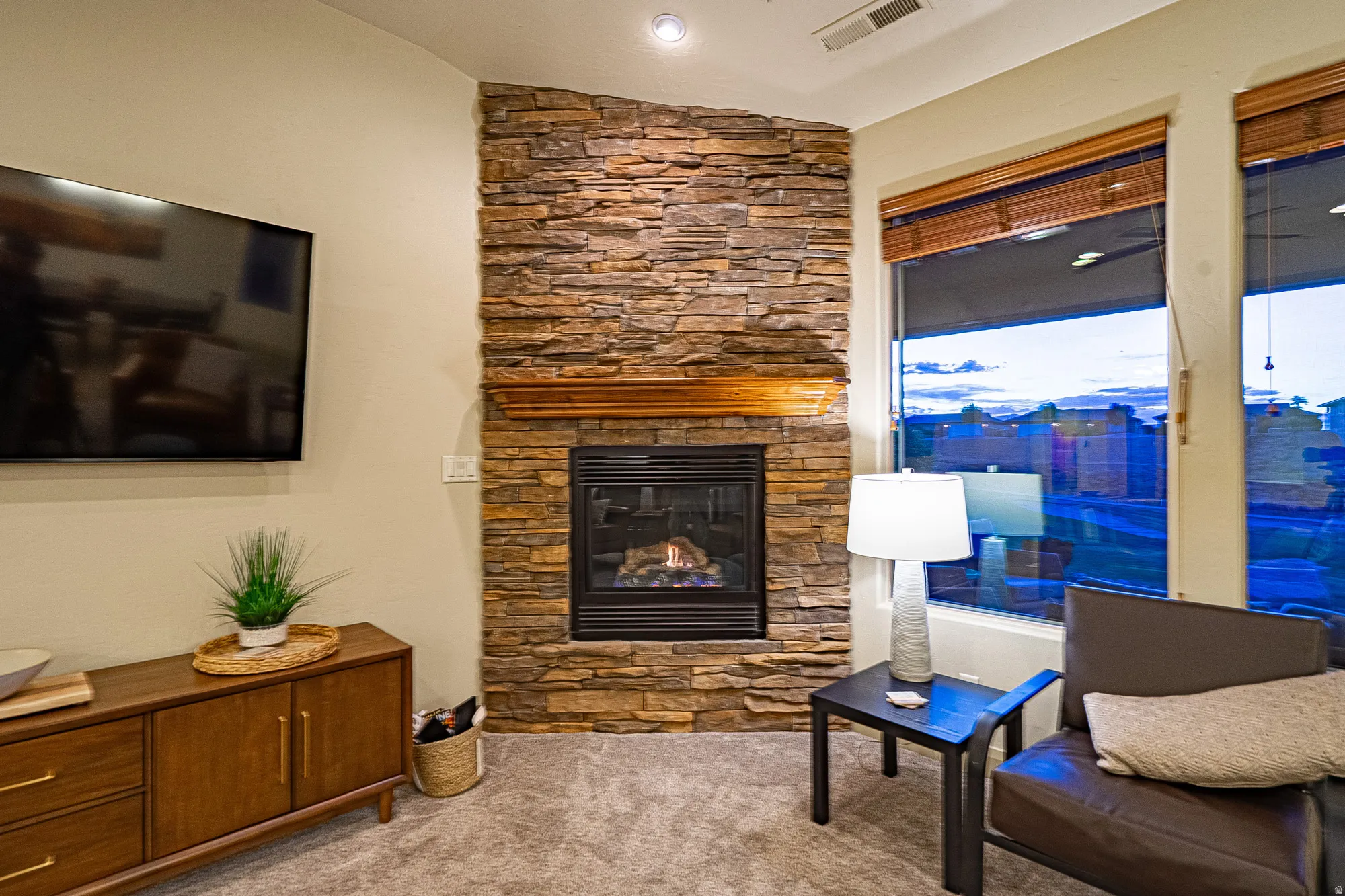 Living area with a stone fireplace, light colored carpet, and lofted ceiling
