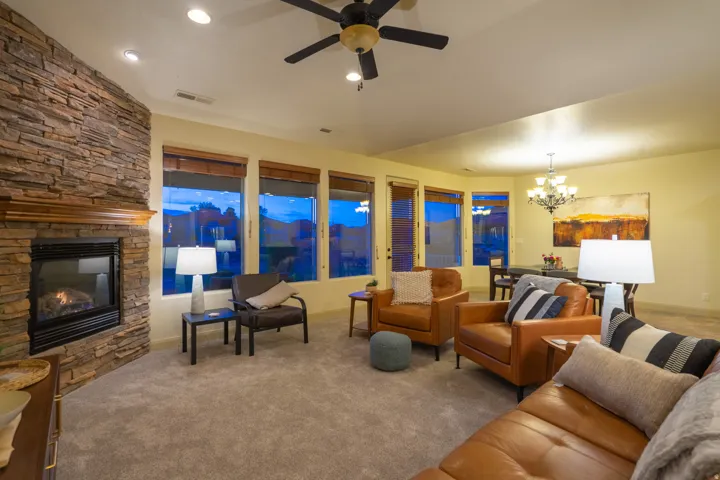Carpeted living area with suspended lighting, a ceiling fan, and a stone fireplace