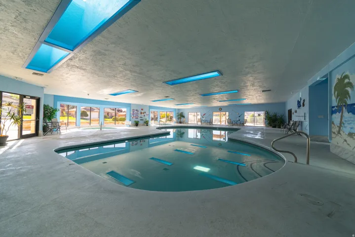 Indoor community pool featuring a jacuzzi and a skylight