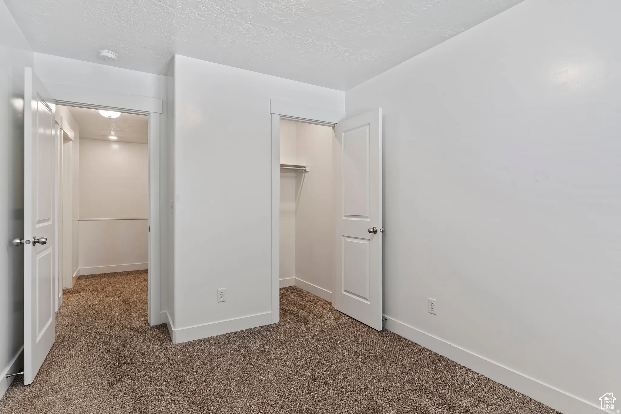Unfurnished bedroom with dark carpet, a spacious closet, and a textured ceiling