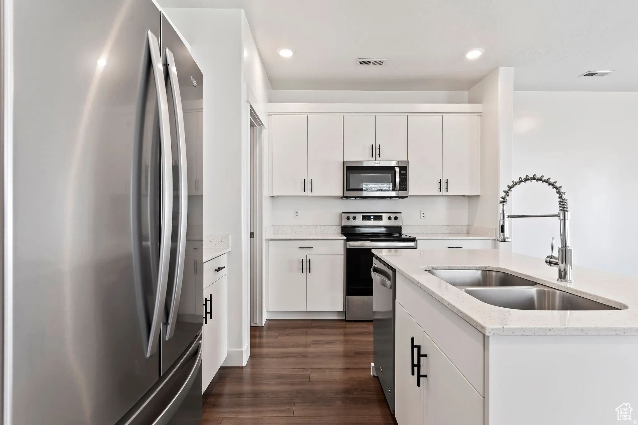 Kitchen featuring stainless steel appliances, dark wood-style floors, light stone countertops, recessed lighting, and white cabinets