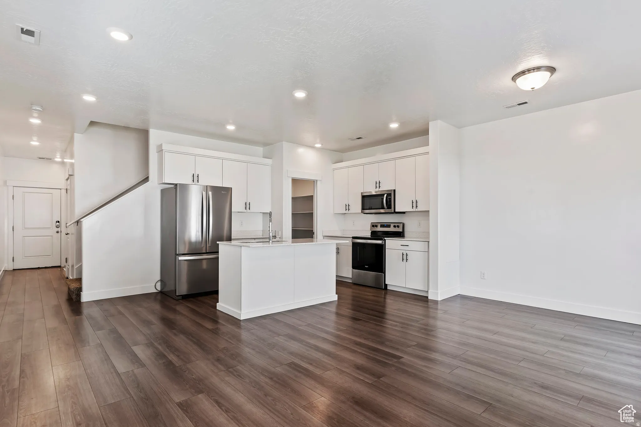 Kitchen featuring stainless steel appliances, white cabinets, dark wood-style floors, an island with sink, and recessed lighting