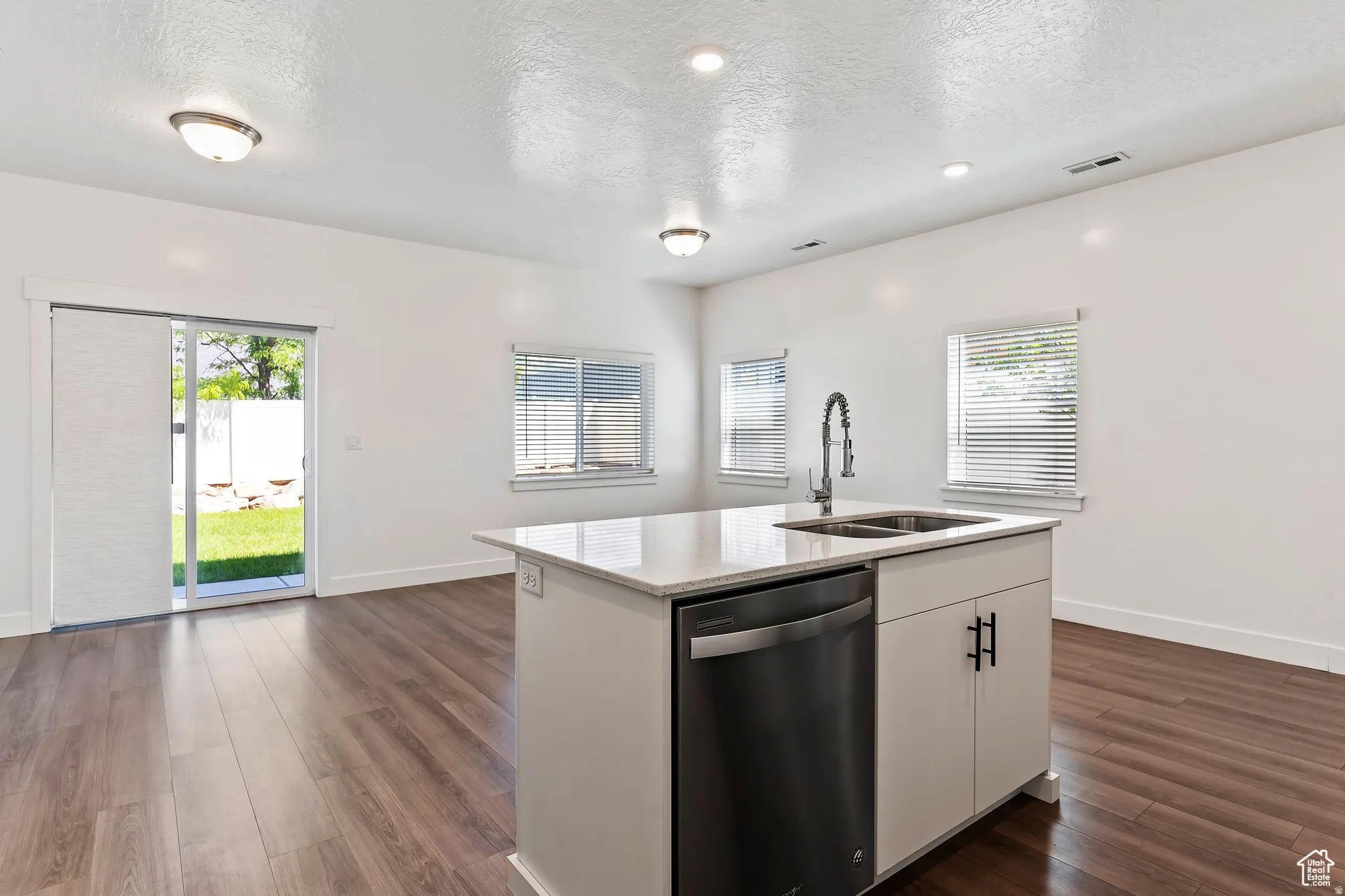Kitchen with dishwasher, white cabinets, light stone countertops, a textured ceiling, and dark wood-style floors
