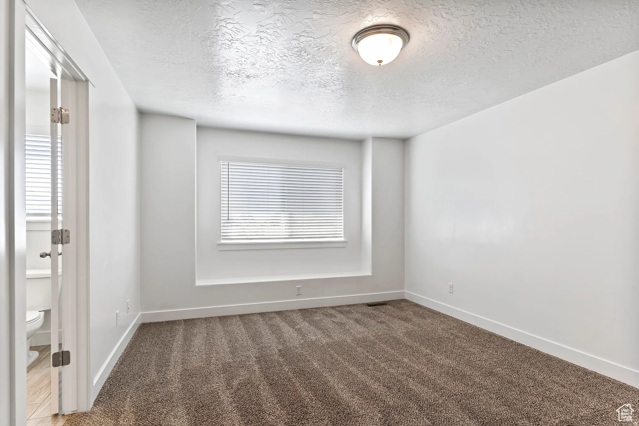 Unfurnished room with a textured ceiling and dark colored carpet