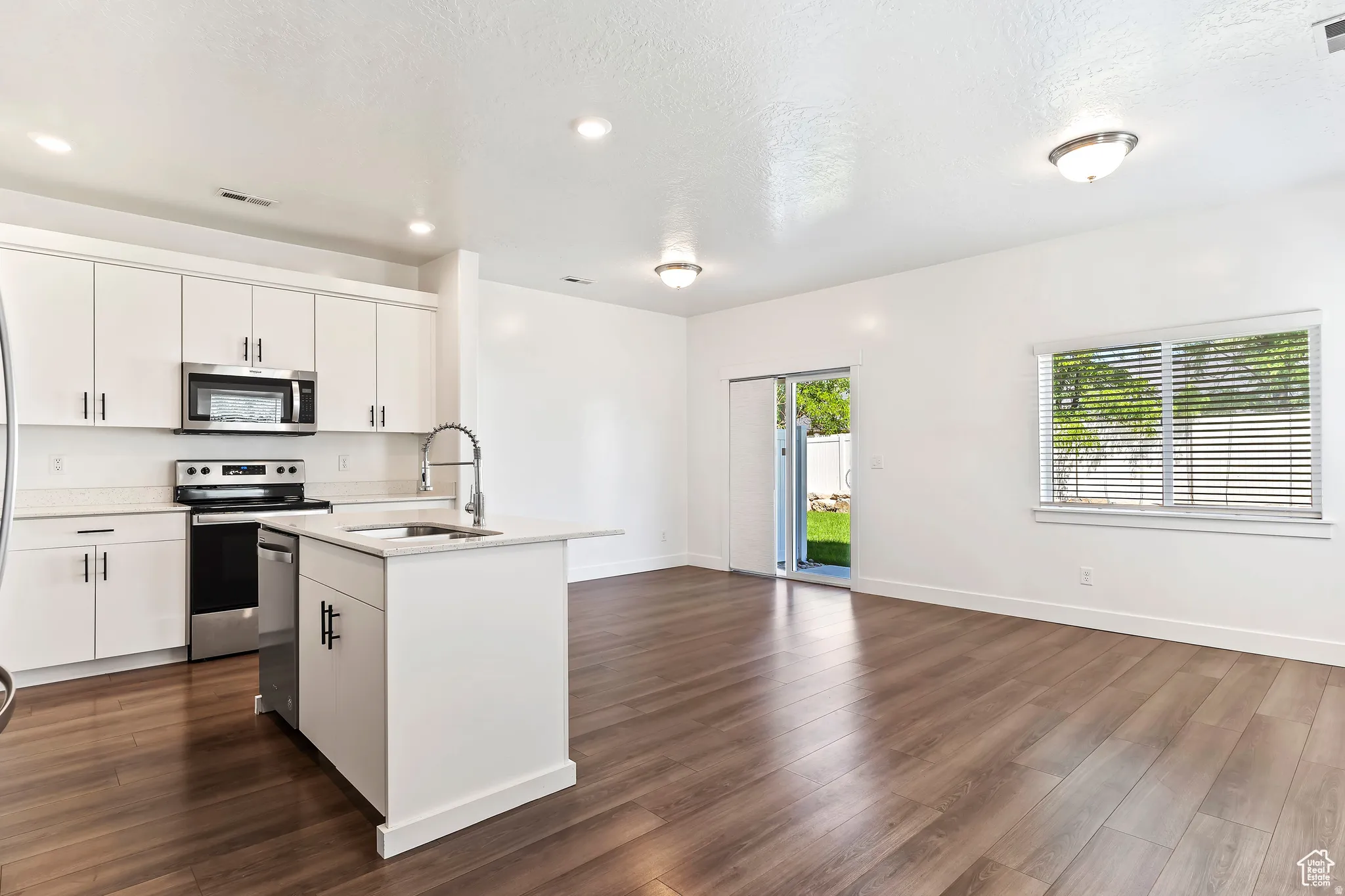 Kitchen featuring an island with sink, stainless steel appliances, white cabinetry, dark wood finished floors, and a textured ceiling