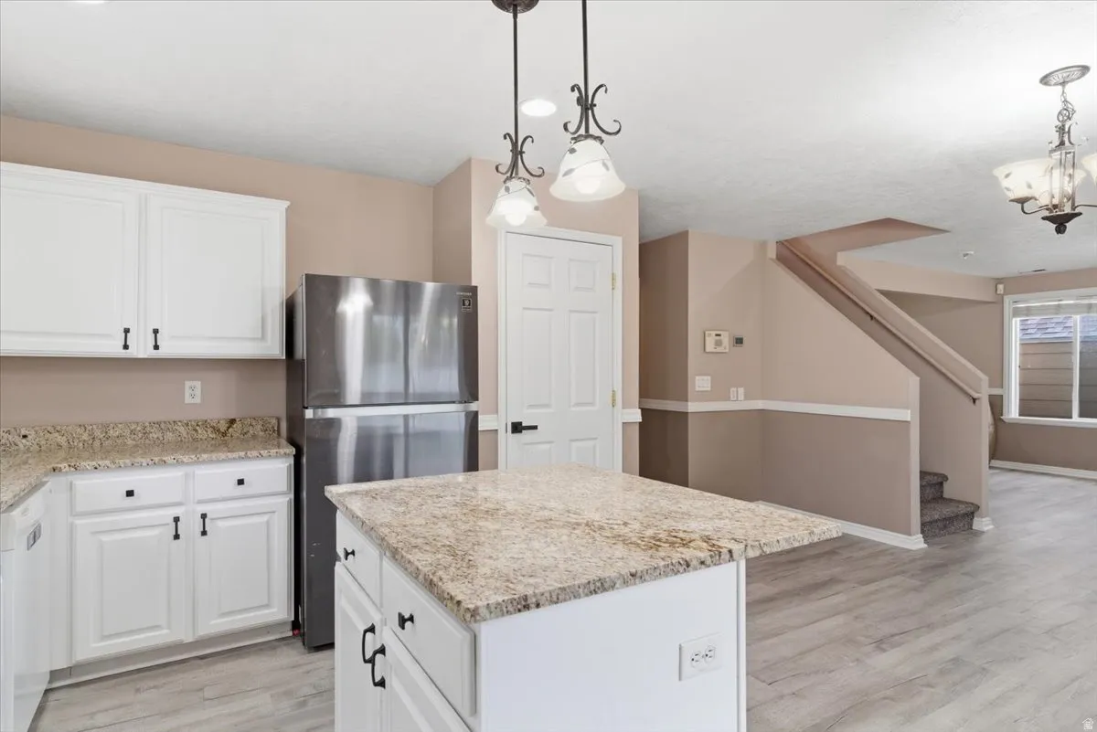 Kitchen with freestanding refrigerator, white cabinetry, a kitchen island, light stone countertops, and light wood-style flooring