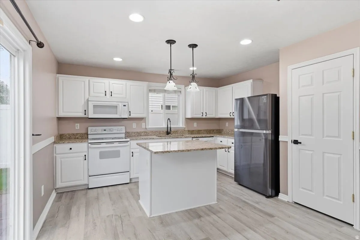 Kitchen with white appliances, white cabinetry, and light stone counters