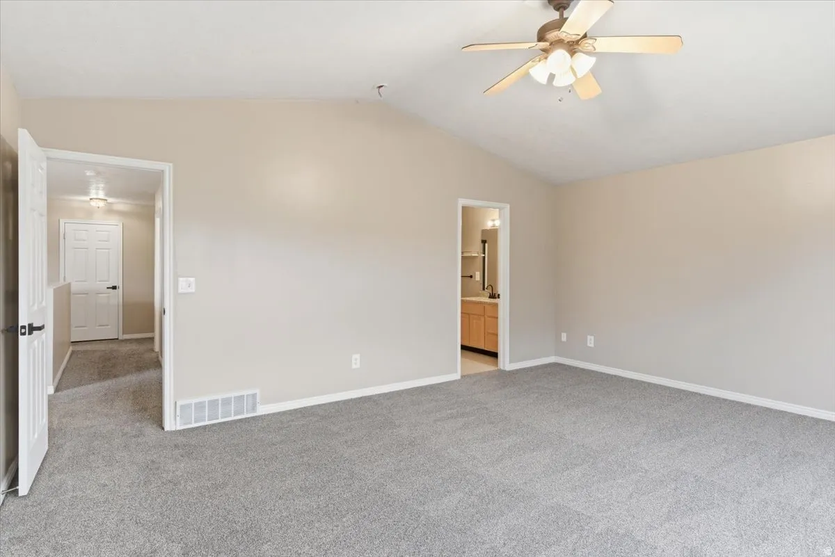 Unfurnished bedroom with light carpet, ensuite bath, and ceiling fan