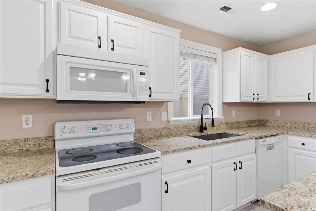 Kitchen featuring white appliances, light stone counters, and white cabinets