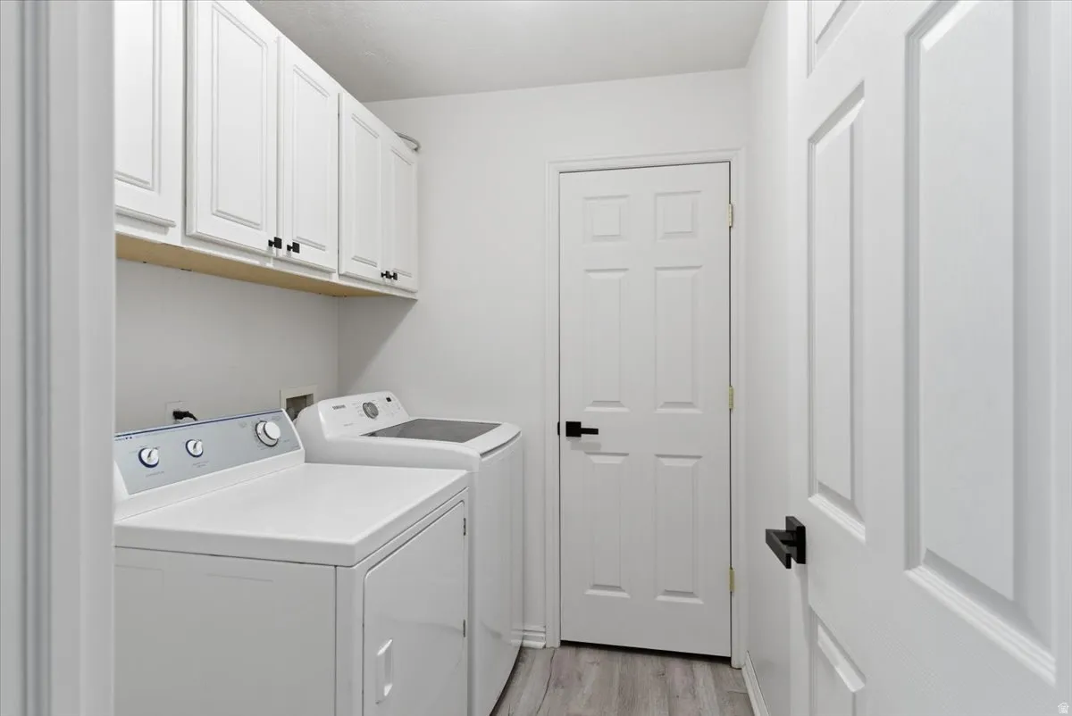 Laundry area with cabinet space, light wood-style flooring, and washing machine and clothes dryer
