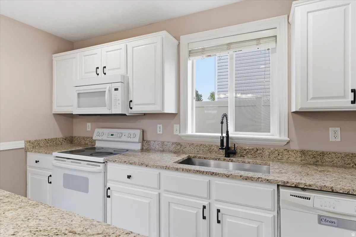 Kitchen with white appliances, white cabinetry, and light stone counters