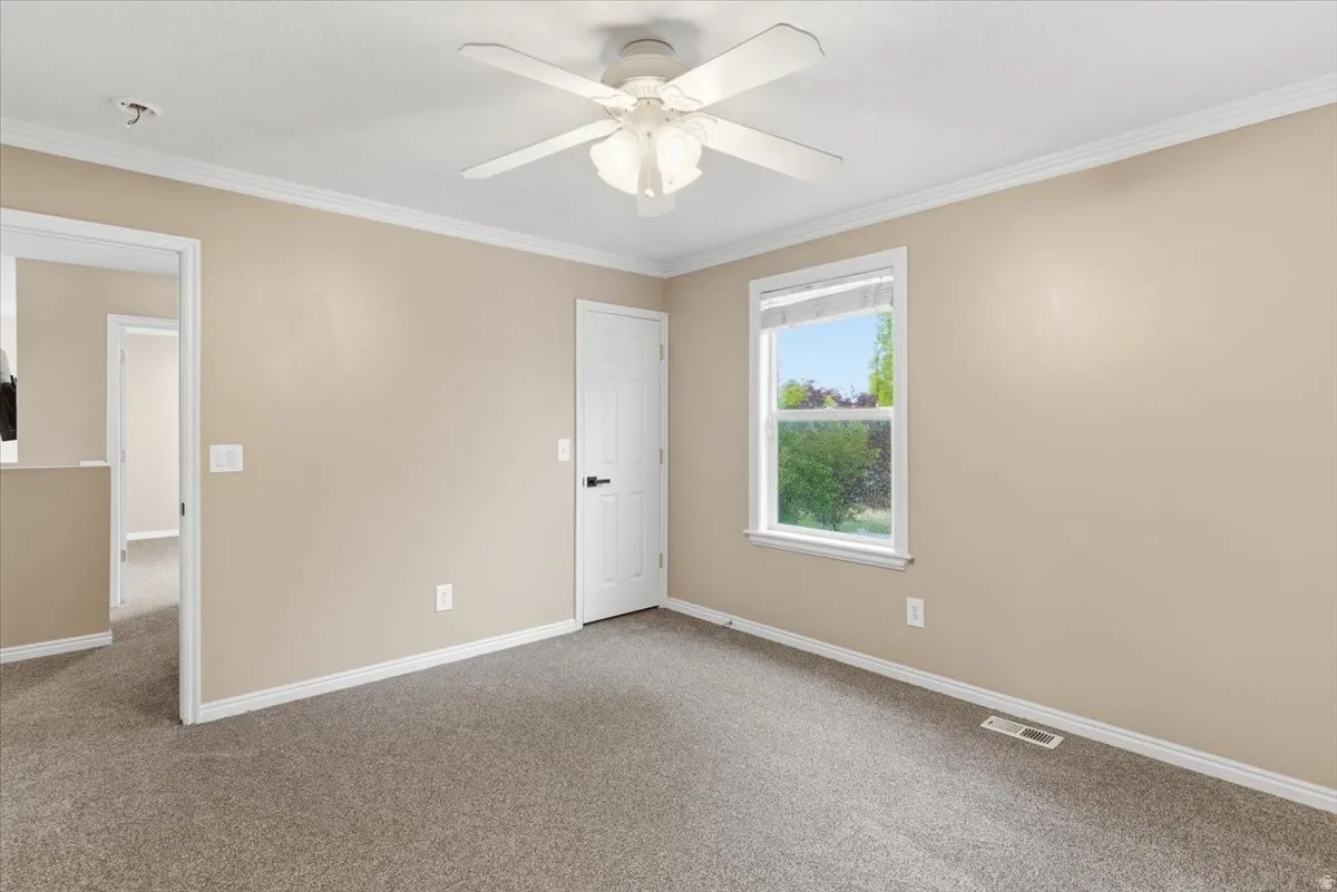 Unfurnished bedroom with crown molding, carpet floors, and a ceiling fan