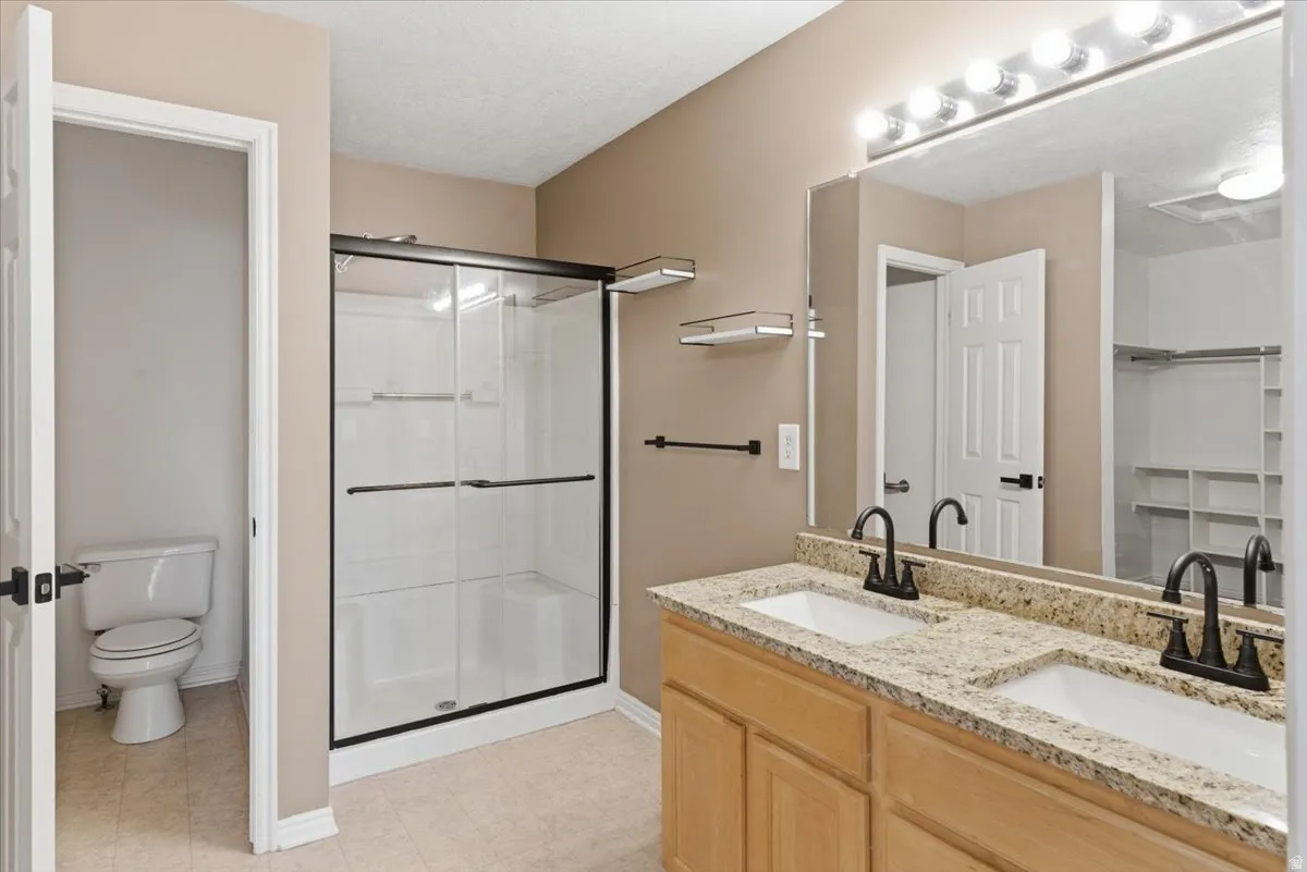 Full bath with double vanity, a shower stall, and a textured ceiling