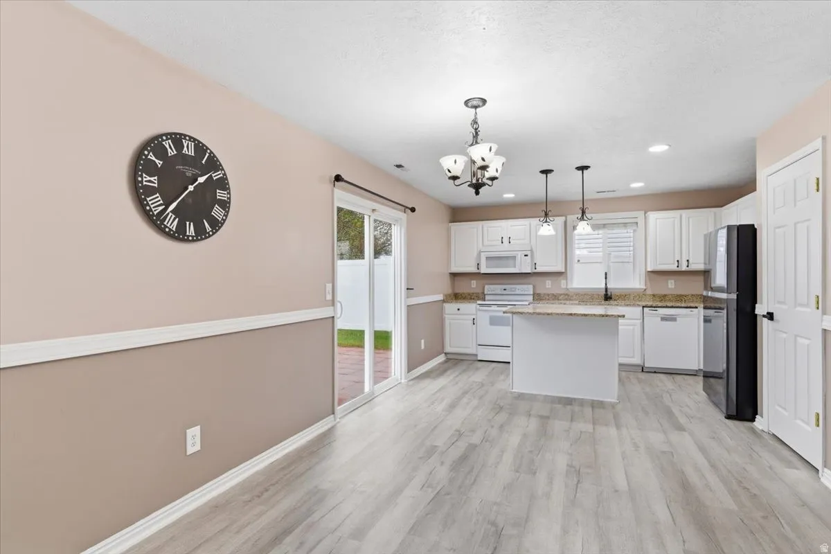 Kitchen with white cabinets, suspended lighting, white appliances, light stone counters, and light wood-style flooring