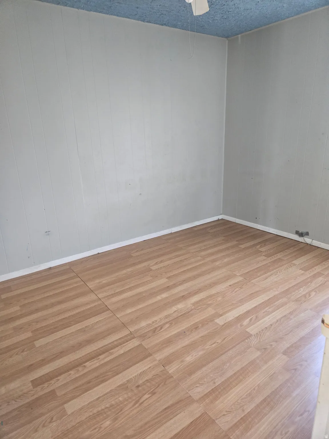 Spare room with light wood-style flooring, a textured ceiling, wooden walls, and a ceiling fan
