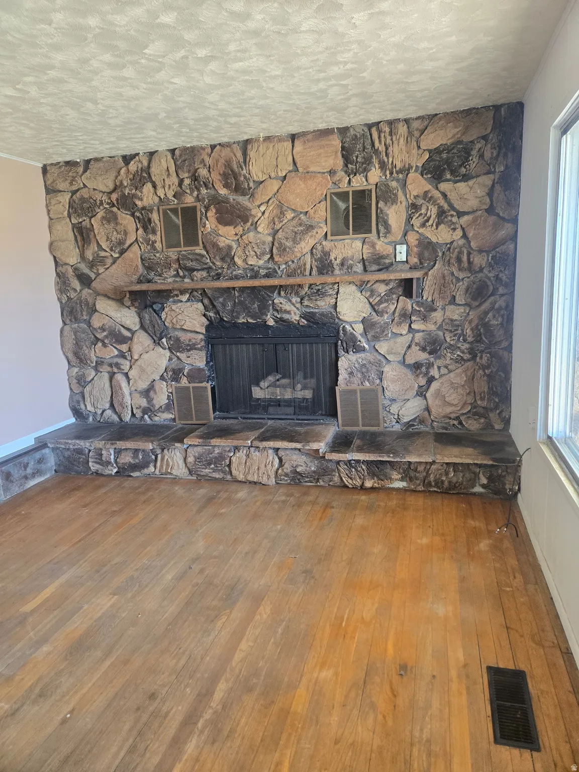 Detailed view of wood finished floors, a stone fireplace, and a textured ceiling