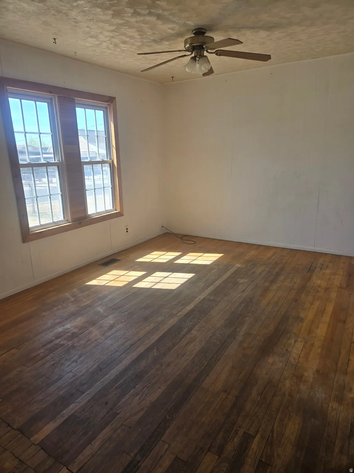 Spare room with dark wood finished floors, a ceiling fan, wooden walls, and a textured ceiling