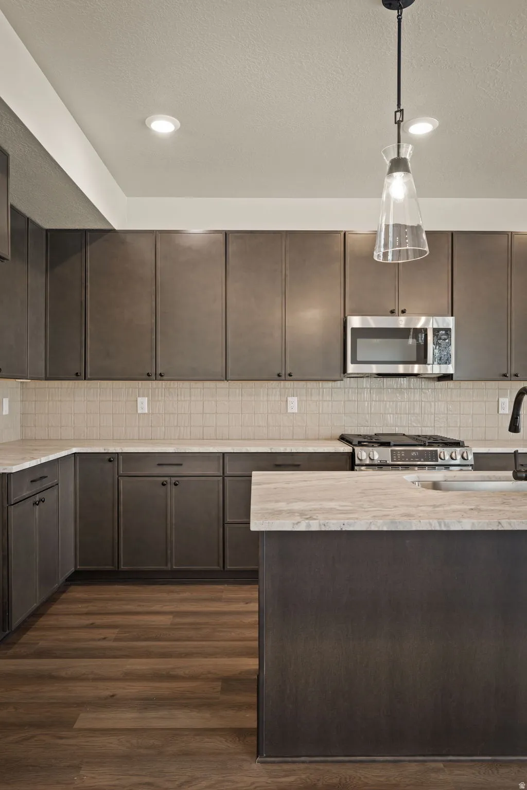 Kitchen with dark wood finish cabinetry, dark wood-style floors, stainless steel appliances, a textured ceiling, and hanging light fixtures