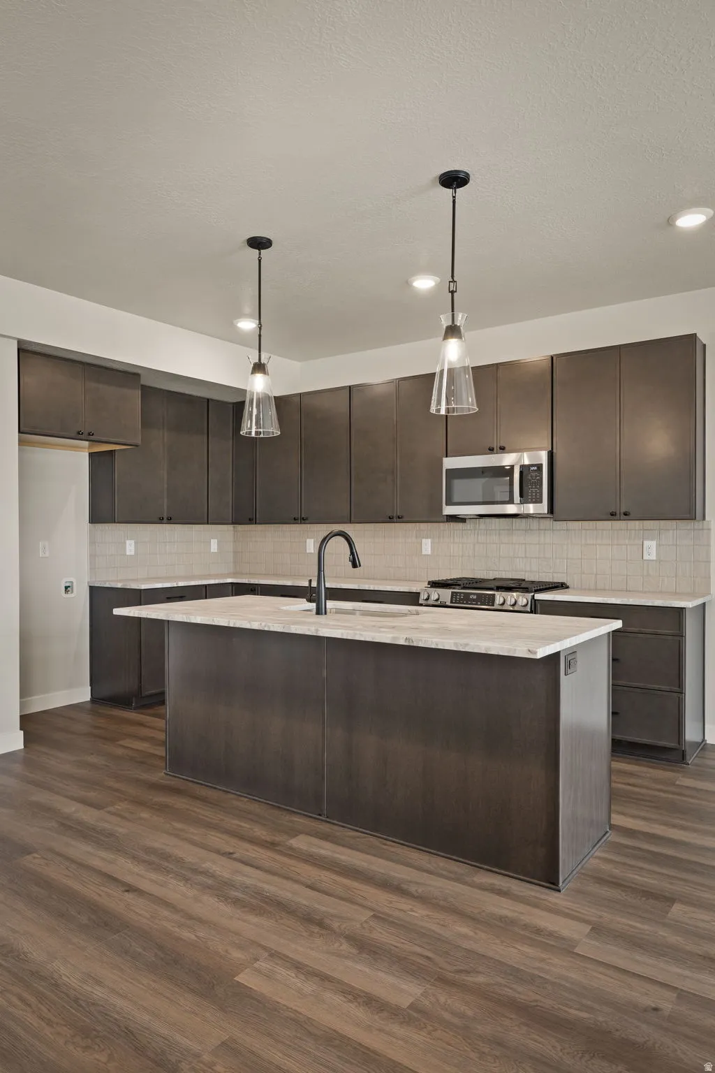 Kitchen featuring dark wood finish cabinets, a kitchen island with sink, decorative light fixtures, and dark wood finished floors