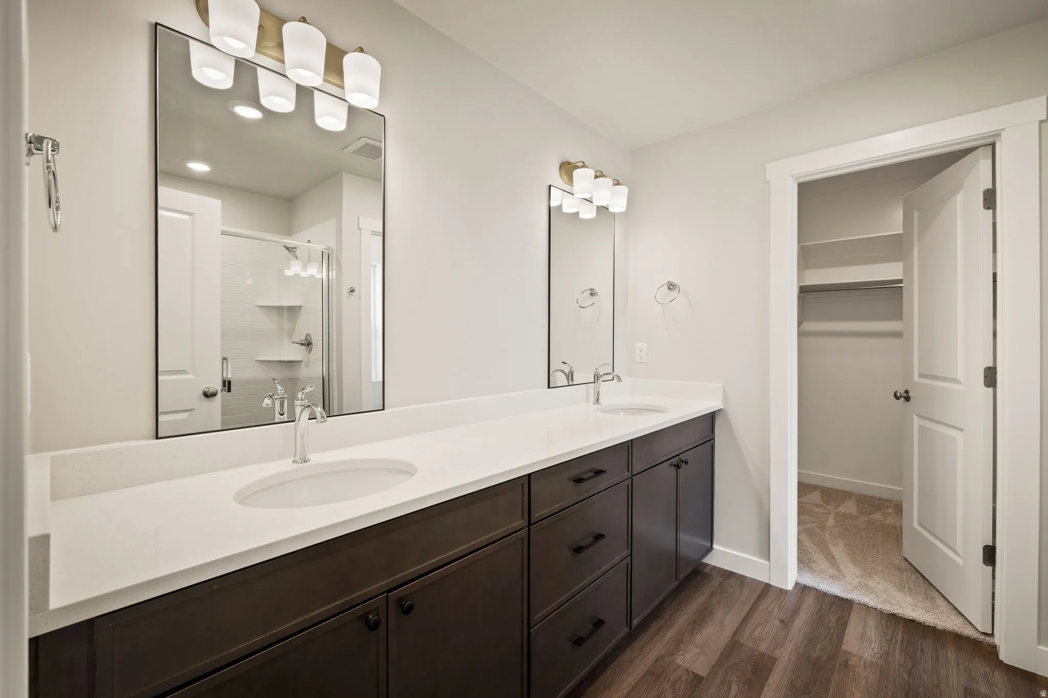Full bathroom with double vanity, a shower stall, dark wood-type flooring, and a spacious closet