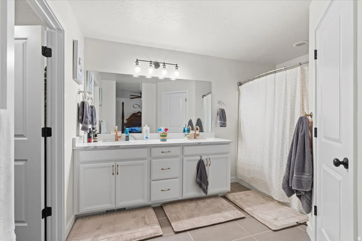 Full bathroom with double vanity, a shower with curtain, a textured ceiling, and light tile patterned floors