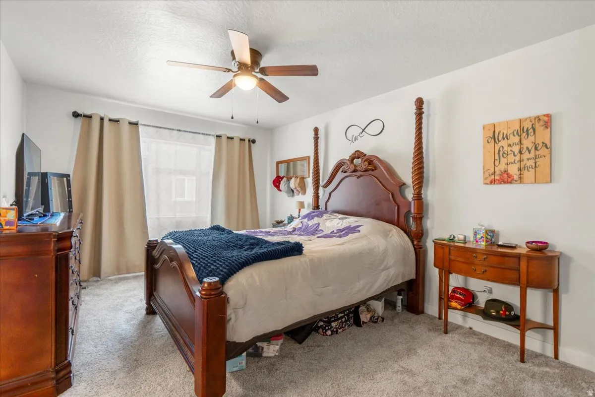 Bedroom with a textured ceiling, a ceiling fan, and light carpet