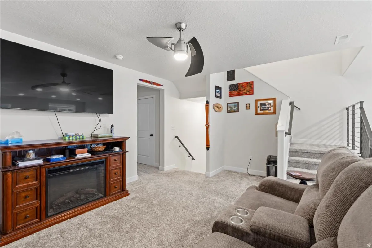 Living room with light colored carpet, ceiling fan, a textured ceiling, and a glass covered fireplace