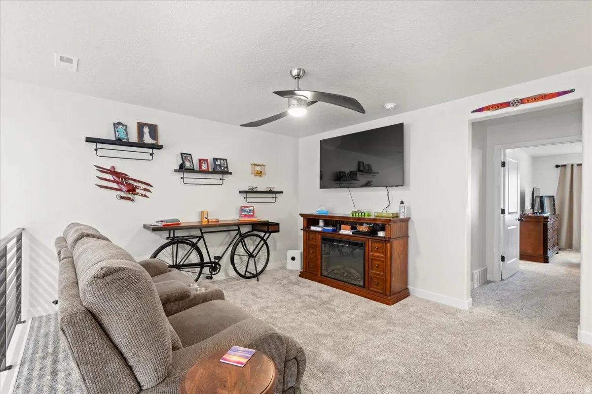 Living area with ceiling fan, light colored carpet, a glass covered fireplace, and a textured ceiling