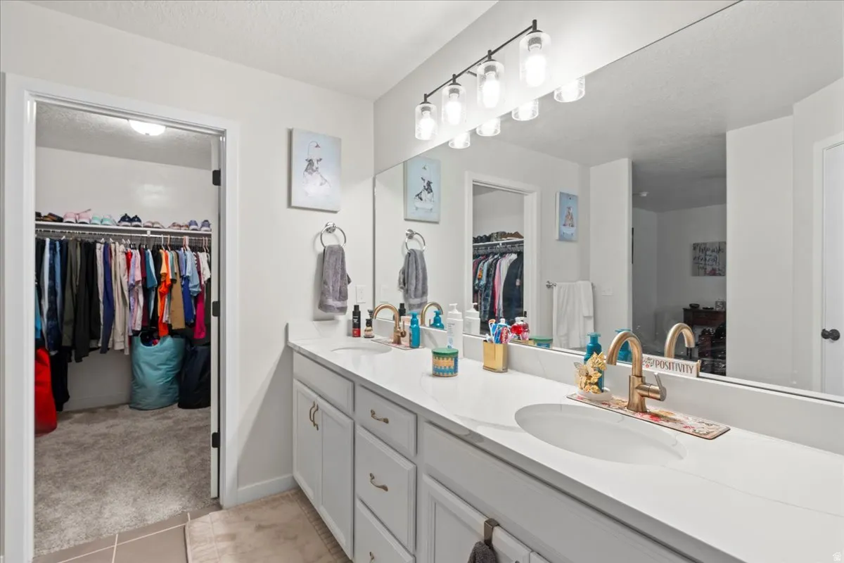 Bathroom with a spacious closet, a textured ceiling, double vanity, light carpet, and light tile patterned floors