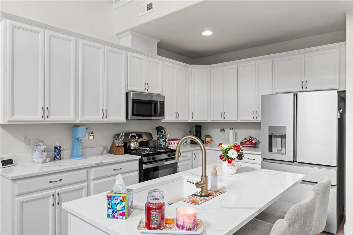 Kitchen featuring stainless steel appliances, white cabinets, a center island with sink, a breakfast bar, and light stone counters