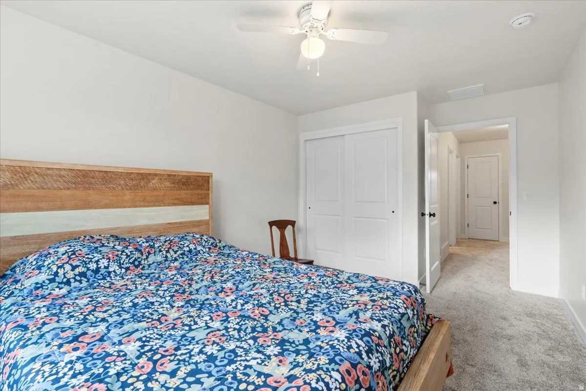 Bedroom featuring light colored carpet, a ceiling fan, and a closet