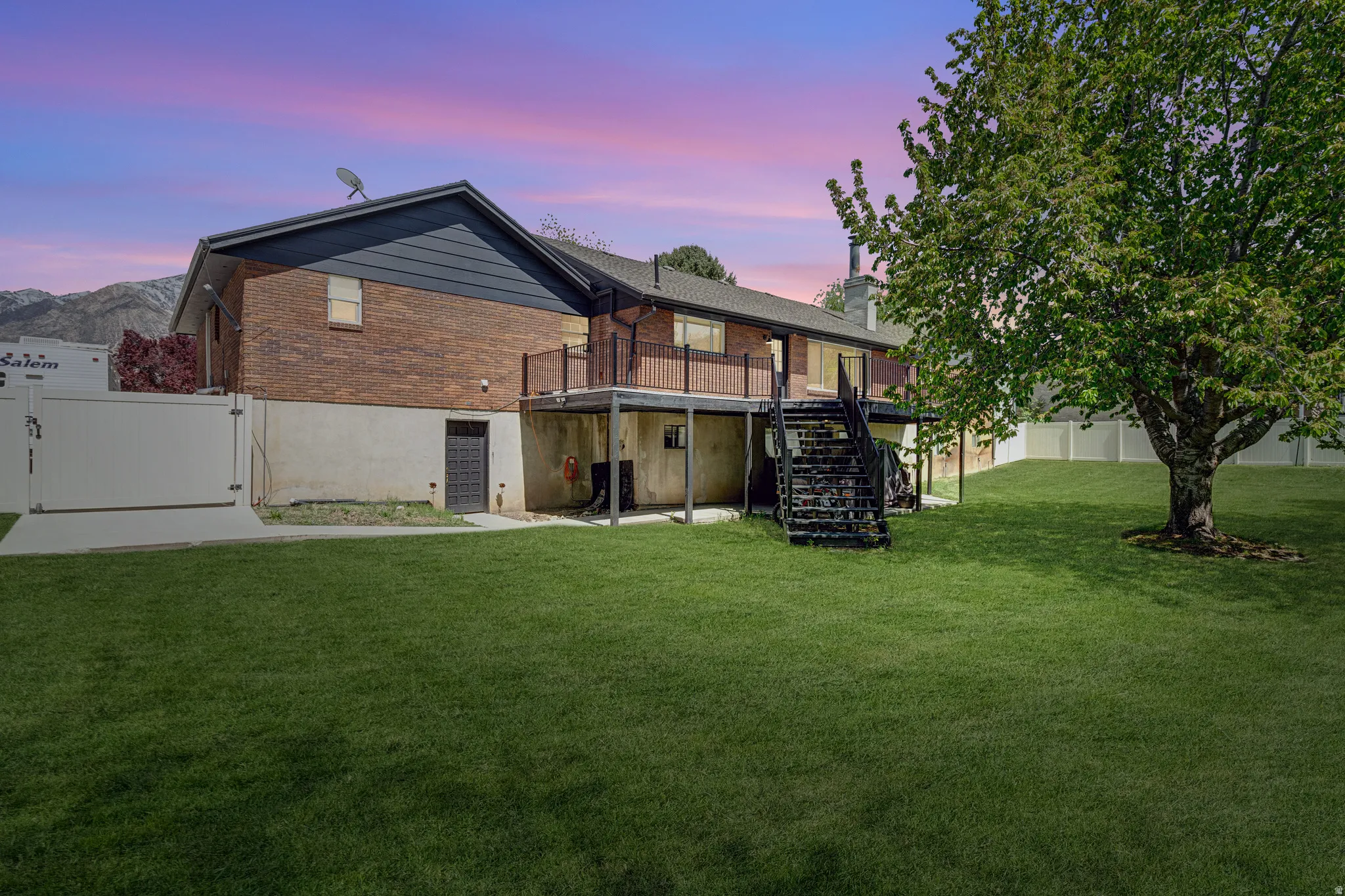 Back of house at dusk featuring a gate, brick siding, a wooden deck, and a chimney
