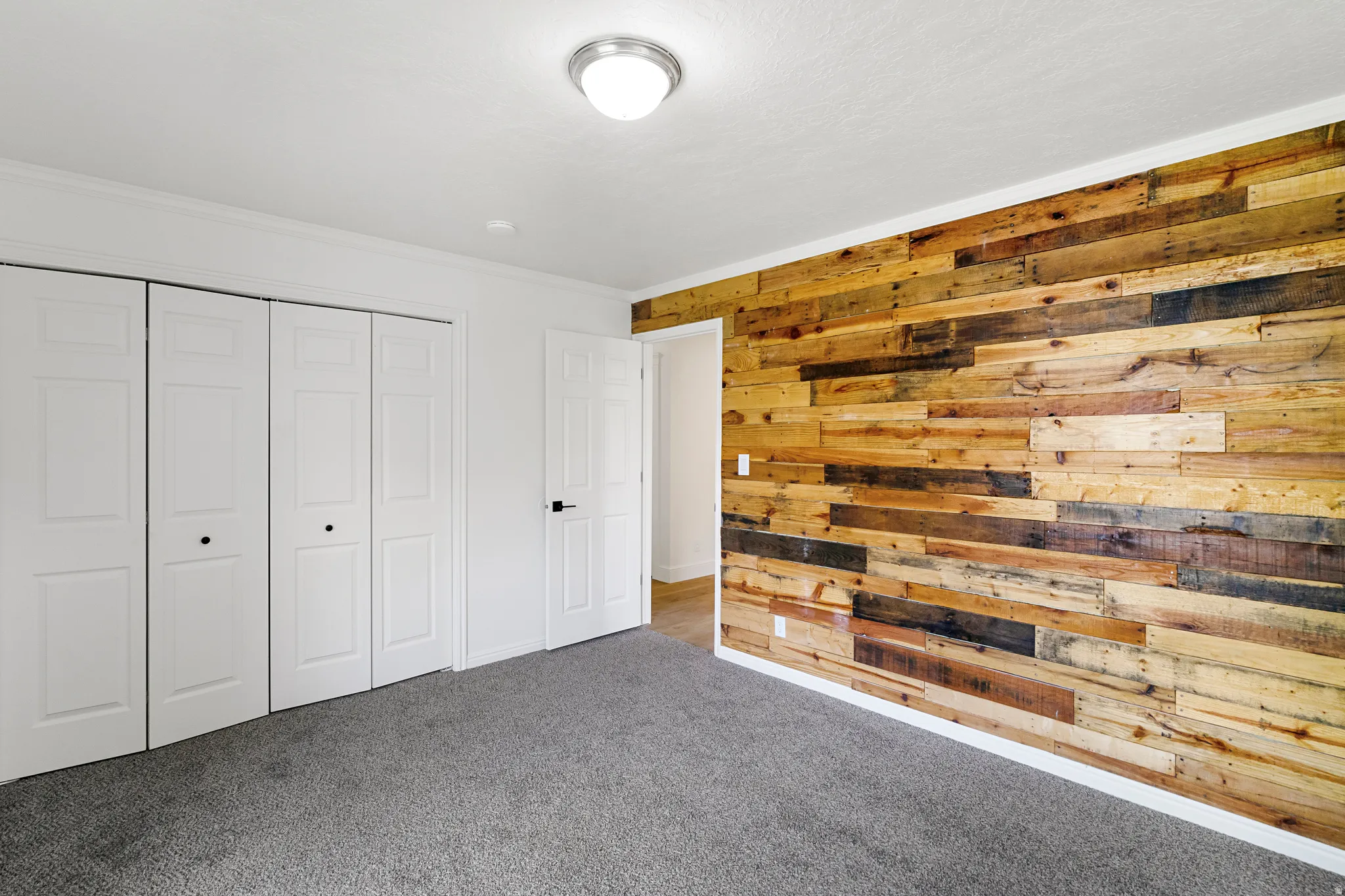 Unfurnished bedroom featuring wood walls, carpet flooring, crown molding, and a closet
