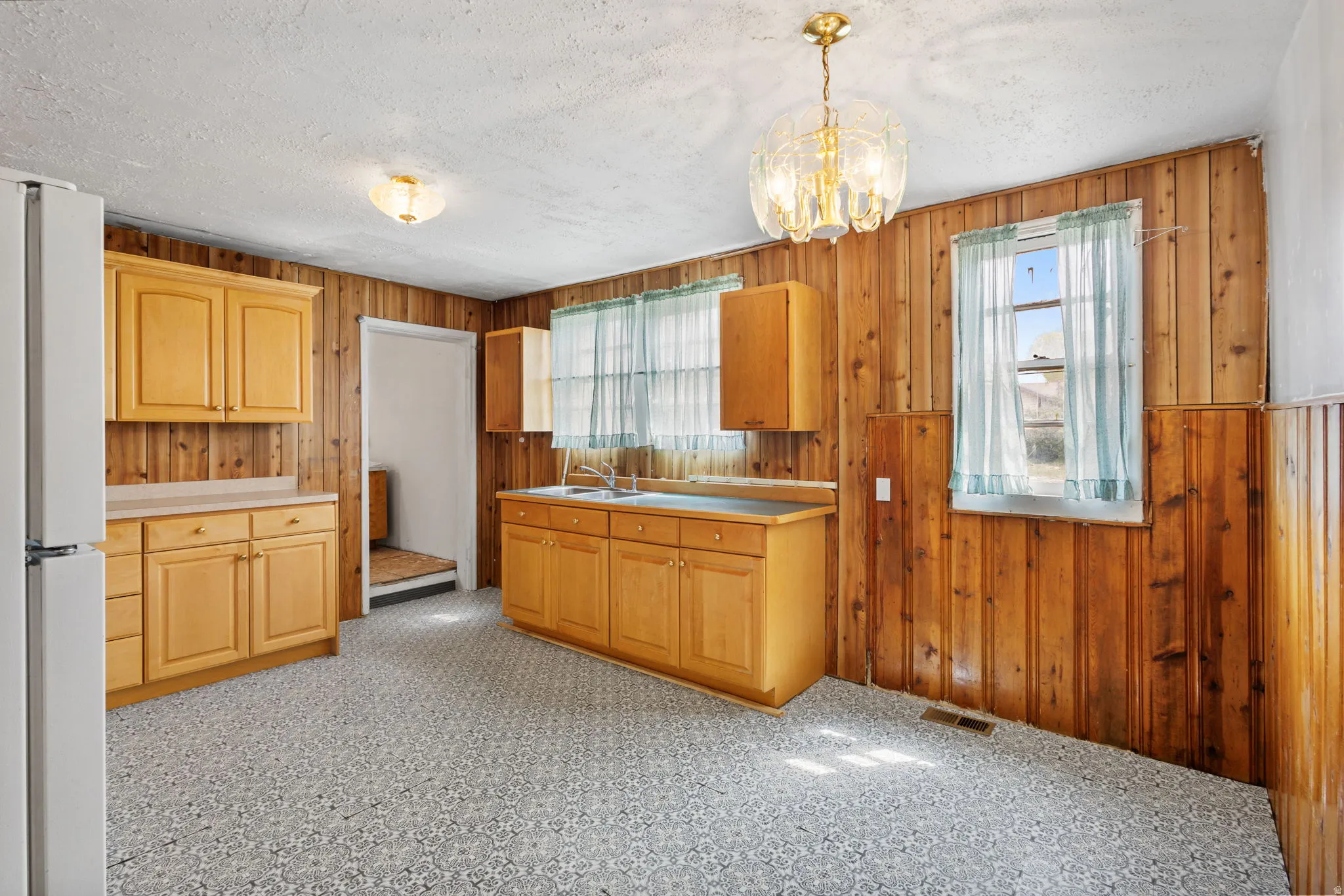 Kitchen with wooden walls, freestanding refrigerator, light countertops, hanging lights, and light flooring
