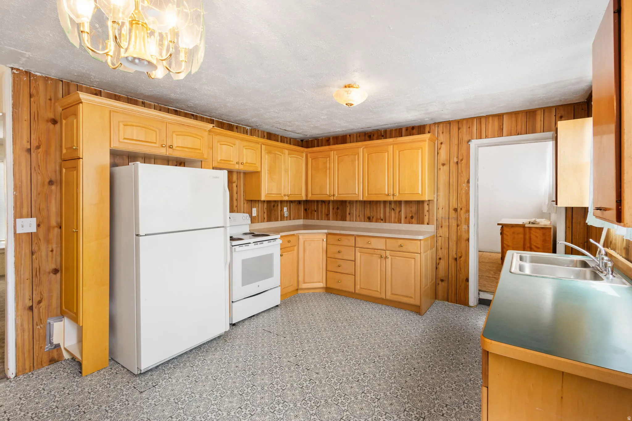Kitchen featuring wood walls, light floors, white appliances, light wood finish cabinets, and a chandelier
