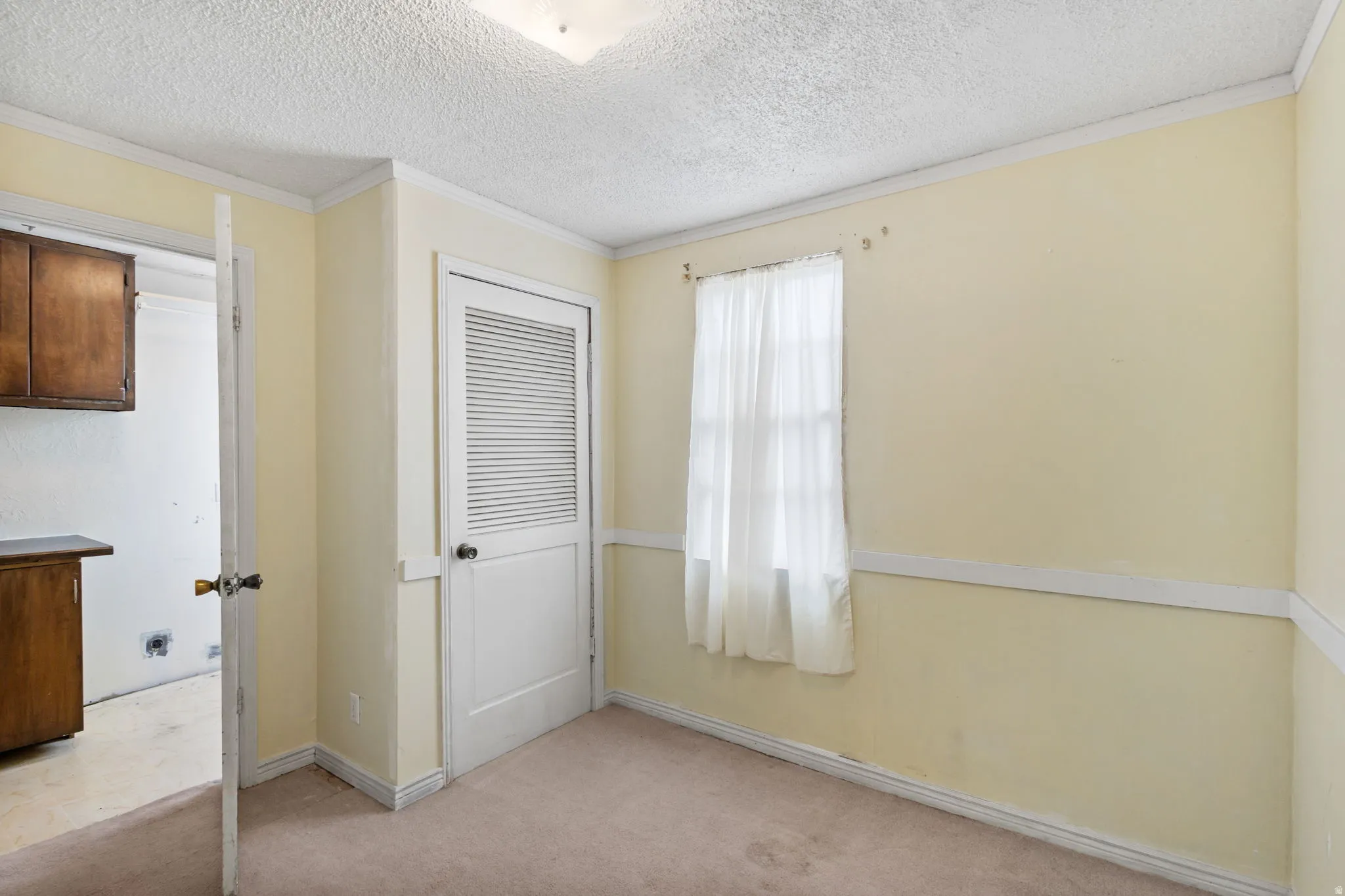 Unfurnished bedroom with light carpet, a textured ceiling, ornamental molding, and a closet