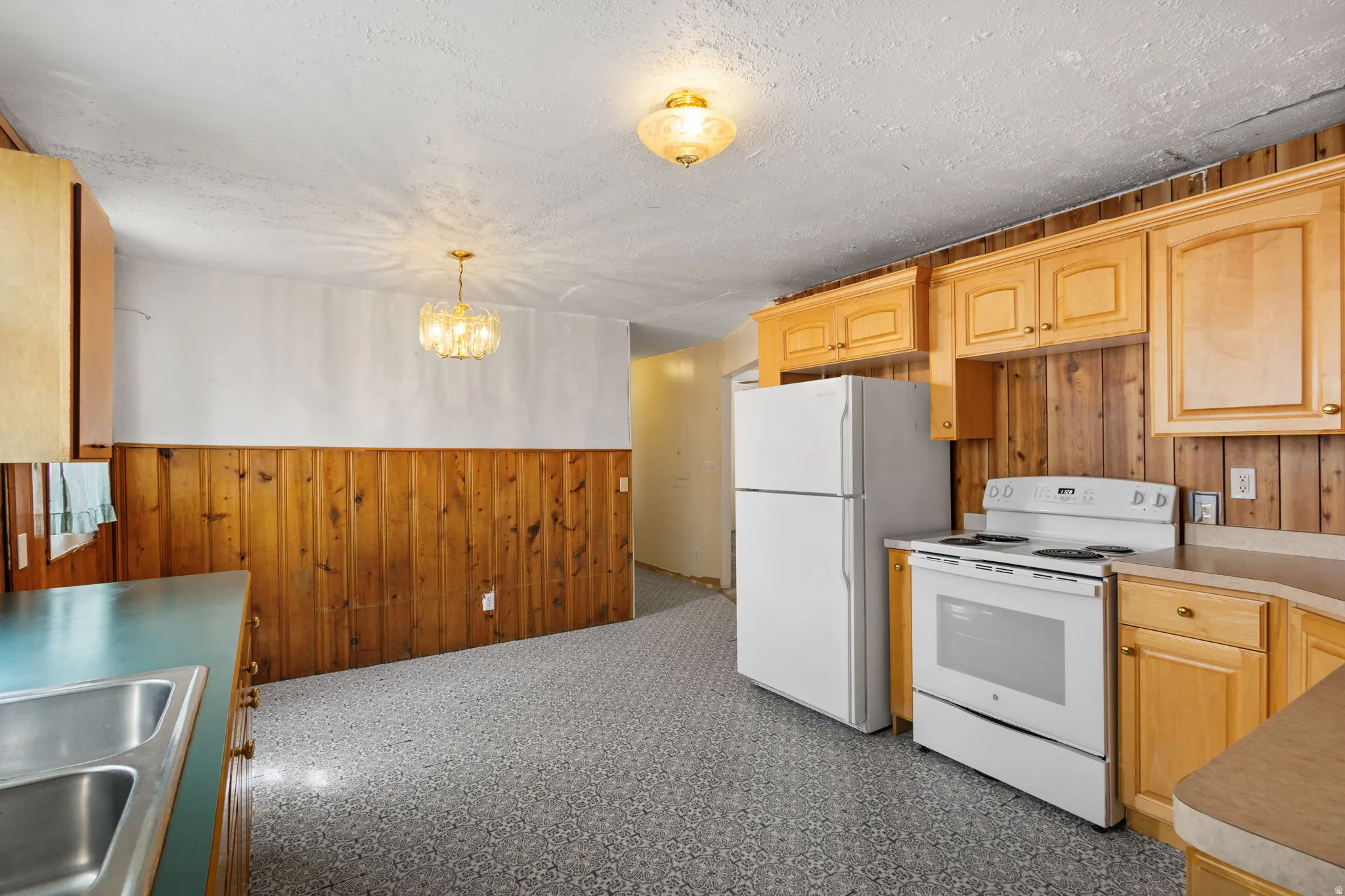 Kitchen with wood walls, a wainscoted wall, white appliances, light wood finish cabinets, and dark floors