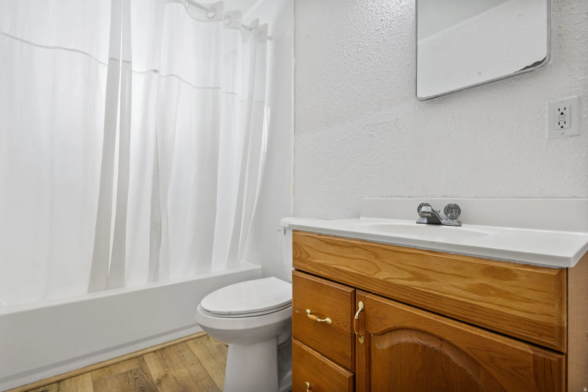 Bathroom with a textured wall, vanity, light wood-style flooring, and shower / tub combo with curtain