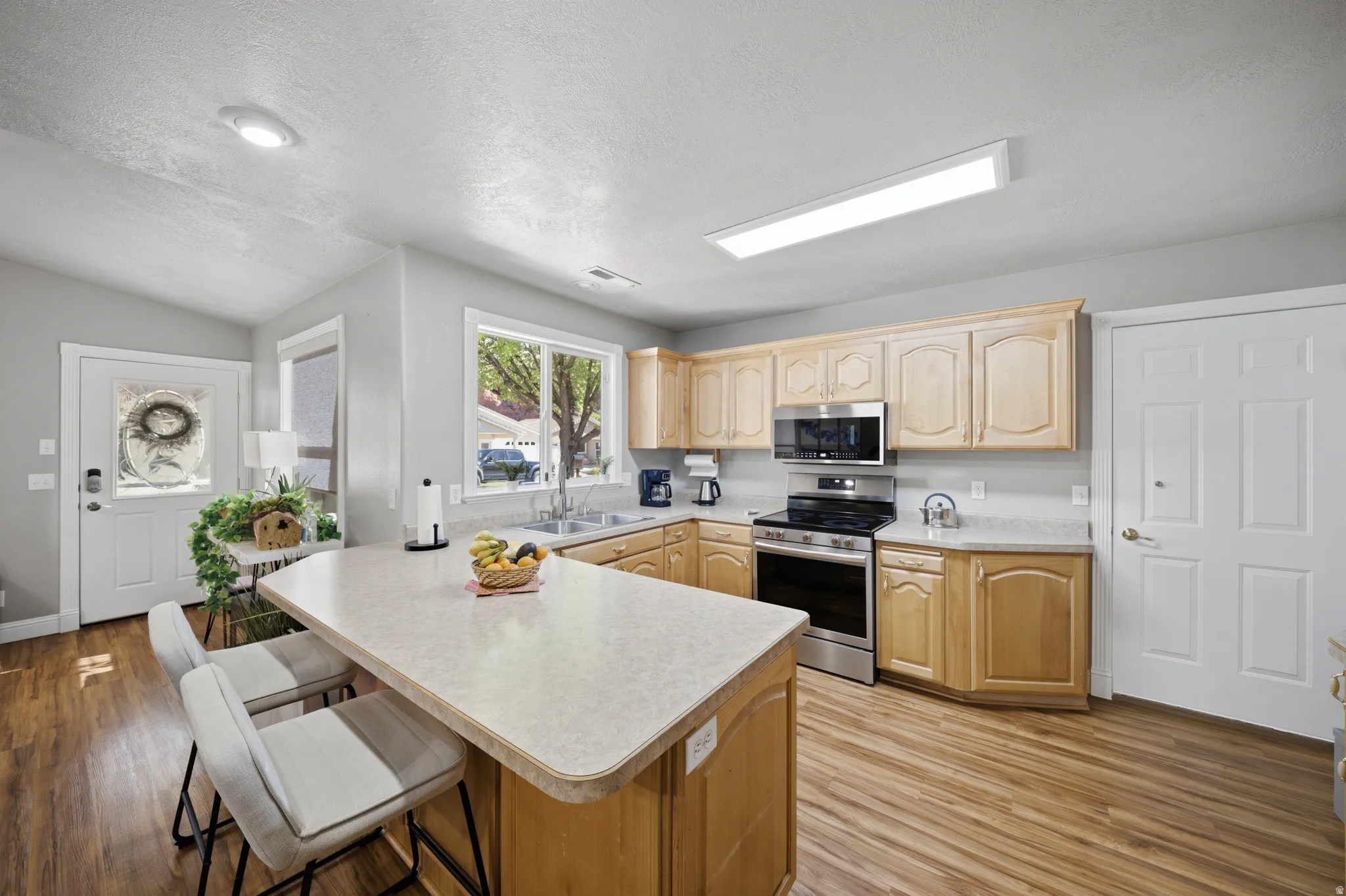 Kitchen featuring light countertops, a kitchen breakfast bar, stainless steel appliances, light wood-style flooring, and a peninsula