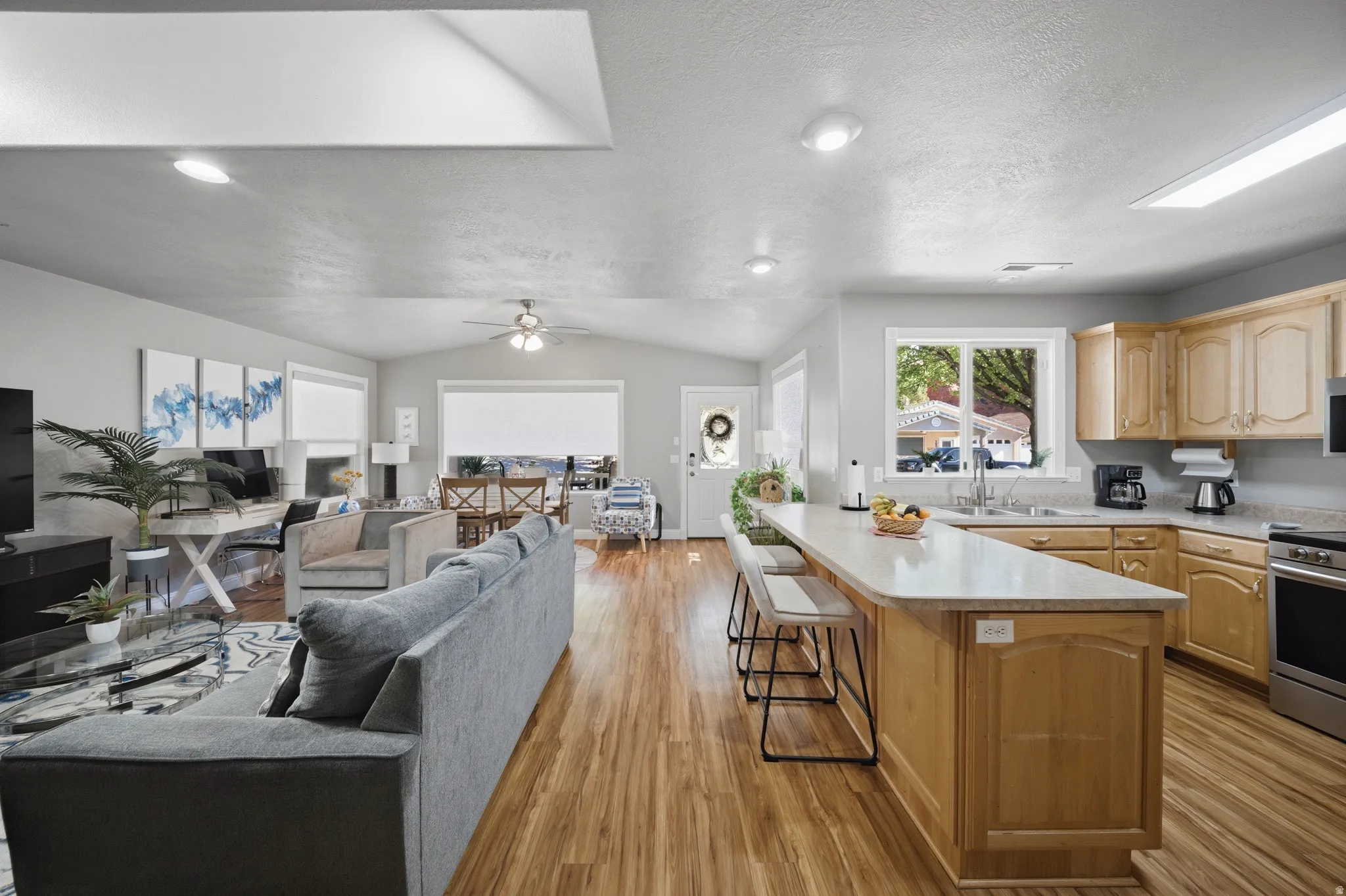 Kitchen with open floor plan, light countertops, light wood finish cabinetry, lofted ceiling, and ceiling fan