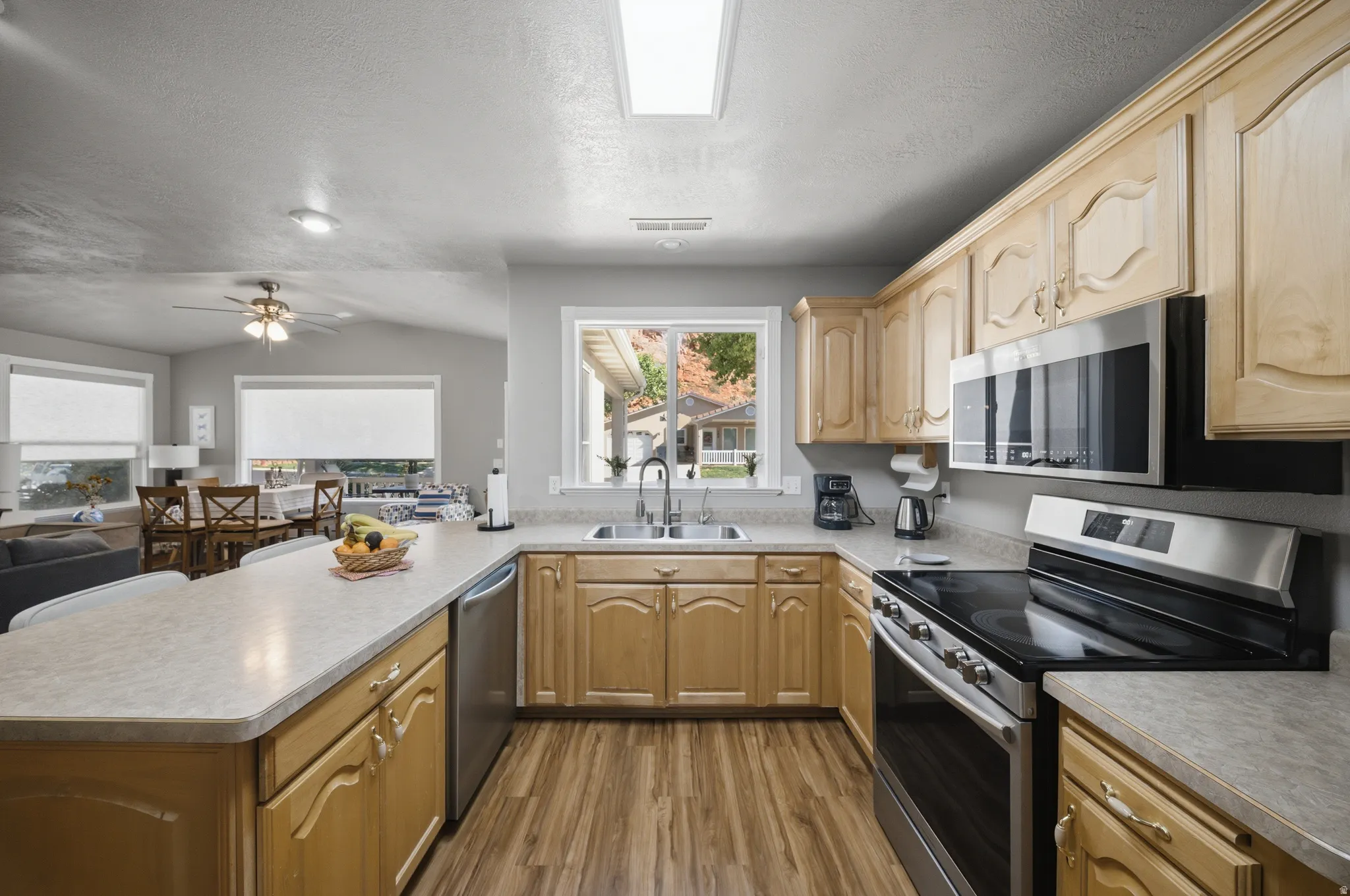 Kitchen with a peninsula, stainless steel appliances, light countertops, light wood finish cabinets, and wood finished floors