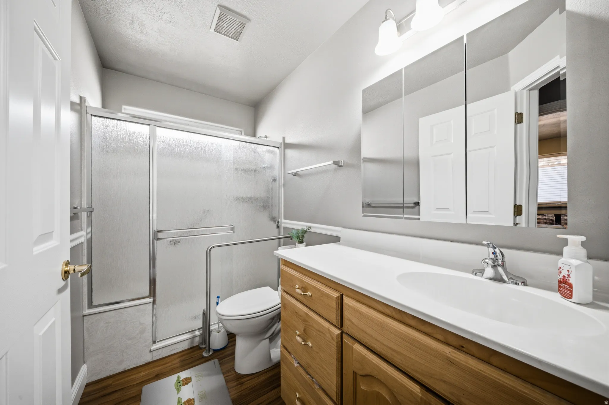 Full bath with a shower with shower door, vanity, and dark wood-style floors