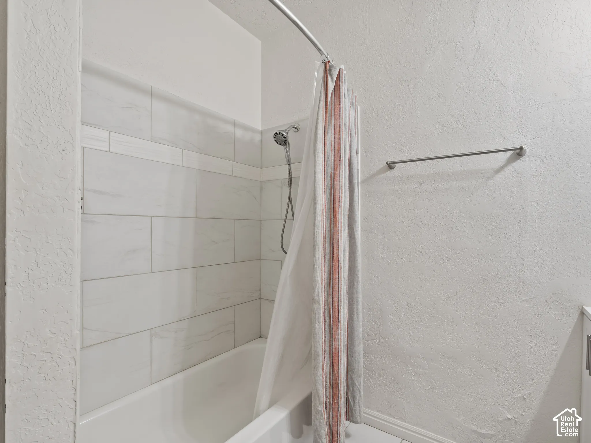 Bathroom with a textured wall, shower / bath combo with shower curtain, and vanity